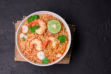 Ramen Instant Noodles in Spicy Shrimp Soup Tom Yum Kung - Asian style food. Placed on a black table with copy space, top view.