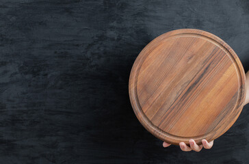 Holding a wooden platter in the hand on black background
