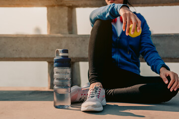 Young asian women sitting to rest after jogging a morning workout in the city.She is holding green...