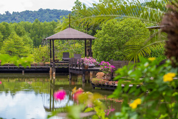 Wooden gazebo with sun loungers for relaxing on a terrace with flowers next to a lake on the tropical island of Thailand