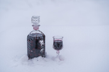 Homemade tincture of red cherry in a glass bottle and a wine crystal glass on a snow and white...