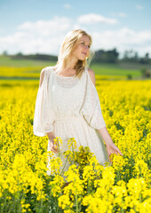 Young woman in yellow oilseed rape field posing in white dress outdoor