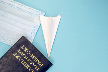 On a blue background a medical face mask and a blue passport with a white paper airplane. Template with workspace