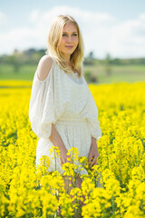 Naklejka na ściany i meble Young female posing in yellow oilseed rape field wearing in white dress outdoor