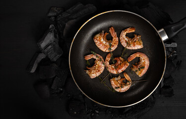Prawns fried with herbs Thyme in a frying pan on a dark background. Seafood appetizer, no people, horizontal orientation, flat lay, top view, copy space