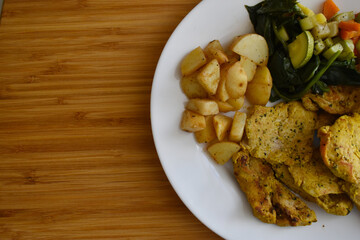 A plate with chicken, potatoes, and vegetables on a wooden table
