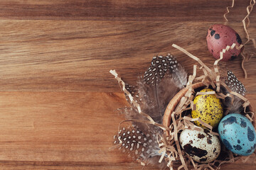 Easter nest made of hay with painted colored eggs and feathers on a wooden background. Flat flat, top view, copy space. Easter background. Easter concept in a traditional retro style