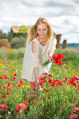 Naklejka na ściany i meble Beautiful young female in white dress holding bouquet of poppy flowers in fields
