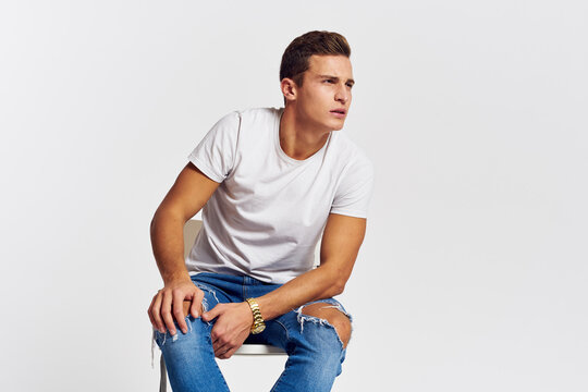 Man on a chair indoors torn jeans white t-shirt handsome face model light background