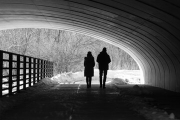 A couple walking together outdoors on a sunny day under a bridge.