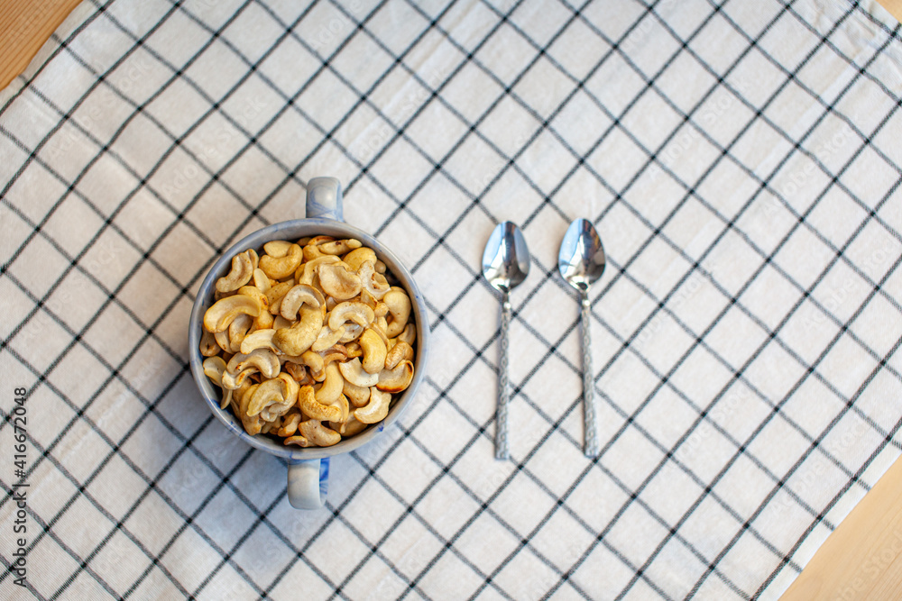 Poster a plate of cashew nuts on a nice napkin and two spoons next to it.