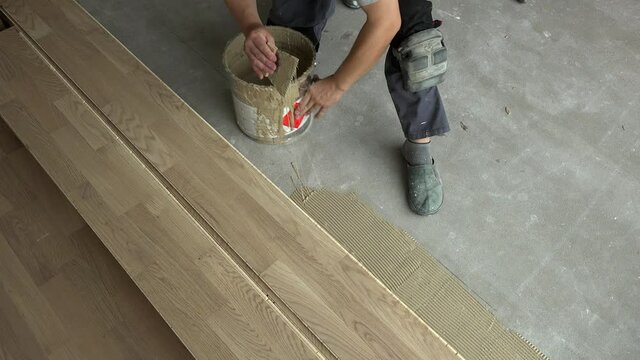 Handyman with spatula apply wood adhesive on concrete floor