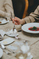 man eats red soup, sits at an elegantly served table in a restaurant, close-up. female hands with a spoon over red soup. borscht closeup