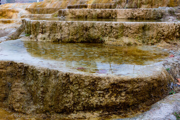 Fototapeta na wymiar Clear warm water in red travertine terraces. Hot springs terraces view