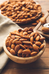 Bowl with tasty almonds on wooden background