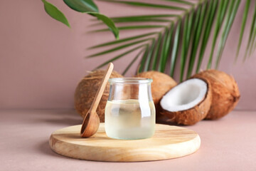 Jar of coconut oil and spoon on color background