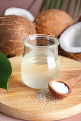 Jar of coconut oil and spoon with flakes on color background