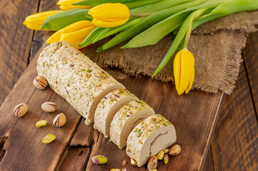 Sliced tahini halva with pistachio on a wooden desk decorated with flowers