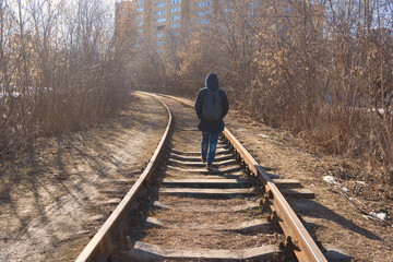 A person in a hood walks along the train tracks