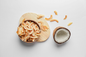Bowl with tasty coconut chips on light background