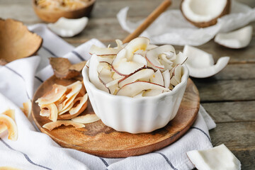 Bowl with tasty coconut chips on wooden background