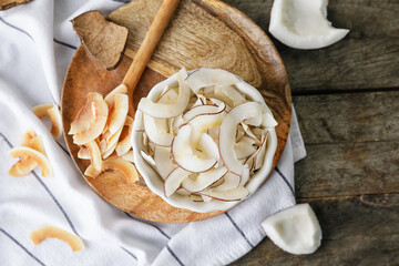 Bowl with tasty coconut chips on wooden background