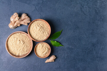 Bowls with ginger powder and roots on color background