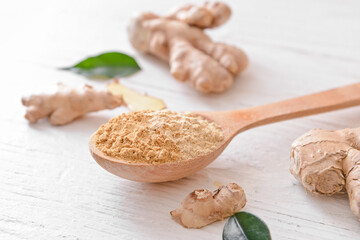Spoon with ginger powder and roots on light wooden background, closeup