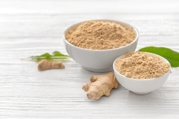 Bowls with ginger powder on light wooden background