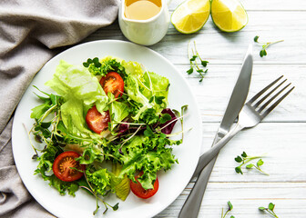 Fresh green mixed  salad bowl with tomatoes and microgreens  on white wooden background. Healthy food, top view.