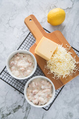 Typisches DDR Würzfleisch Ragout Fin mit geriebenen Gouda Käse in Auflaufform Schale und Zitrone auf Abkühlgitter und Marmor Hintergrund hell