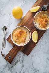 Typisches DDR Würzfleisch Ragout Fin mit geriebenen Gouda Käse überbacken in Auflaufform Schale und Zitrone auf Holzbrett und Marmor Hintergrund hell
