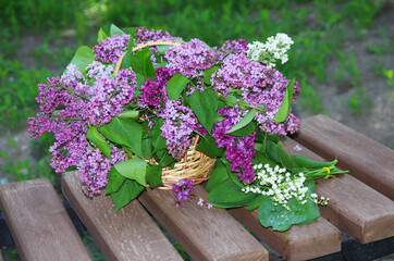 A bouquet of lilacs and a bouquet of lilies of the valley on a garden bench.