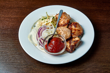 shish kebab with salad and ketchup on a white plate on a dark background