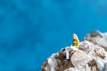 Miniature people Woman wearing headphones and listening to music on smartphone sitting on the rock