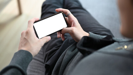 Close up view man holding horizontal smart phone and lying on sofa in living room.