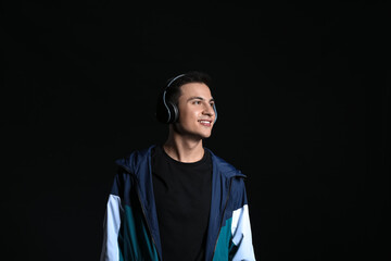 Handsome young man listening to music on dark background