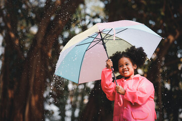 Happy funny child curly black hair with umbrella under the autumn shower. Girl is wearing pink...