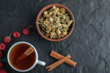 Cup of tea with raspberries and chamomile on black background