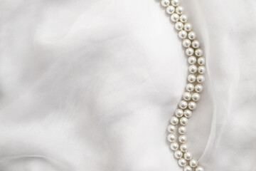 A necklace of pearls lies on a white cloth
