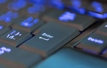Fototapeta na wymiar Closeup of laptop or desktop computer keyboard illumination, blue backlit keyboard. Focus to key enter