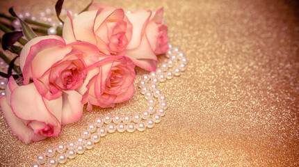 Pink rose and pearl necklace on a shiny gold background
