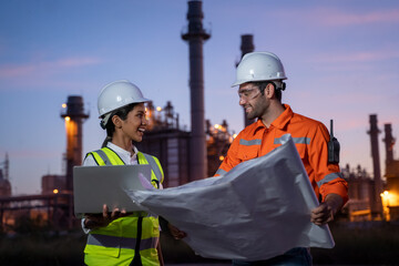 Two engineers working with laptop at front oil and gas refinery plant industry factory.