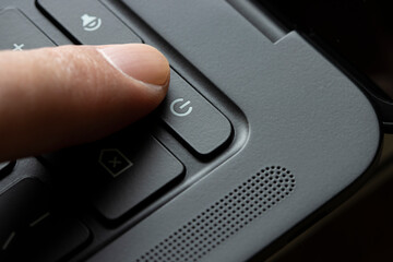 Finger pressing the power button on a black laptop computer.