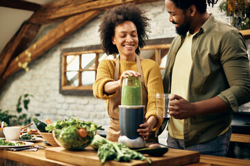 Happy African American couple preparing healthy smoothie in the kitchen. - Powered by Adobe