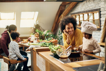Happy African American mother and daughter preparing food in the kitchen.