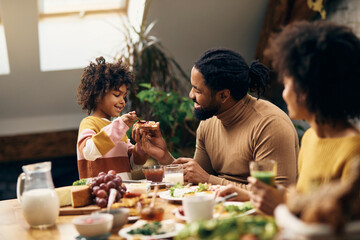 Happy black family eating jam and toasted bread for breakfast at home. - obrazy, fototapety, plakaty