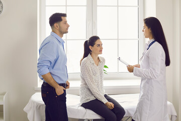 Professional clinician talking to patients. Happy couple planning pregnancy and seeing doctor at good clinic. Future parents listening to gynecologist's advice during health consultation at hospital