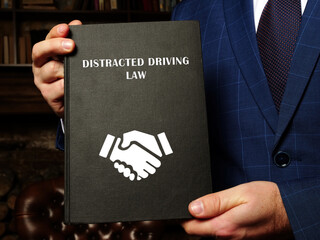  DISTRACTED DRIVING LAW book in the hands of a lawyer. Distracted driving occurs when a driver undertakes any activity that diverts attention away from driving