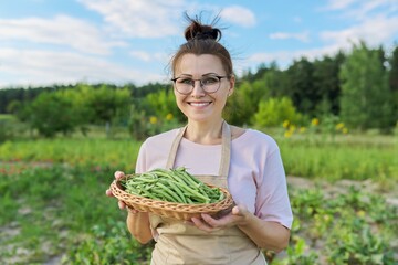 Smiling woman farmer with harvest of fresh green beans in a basket
